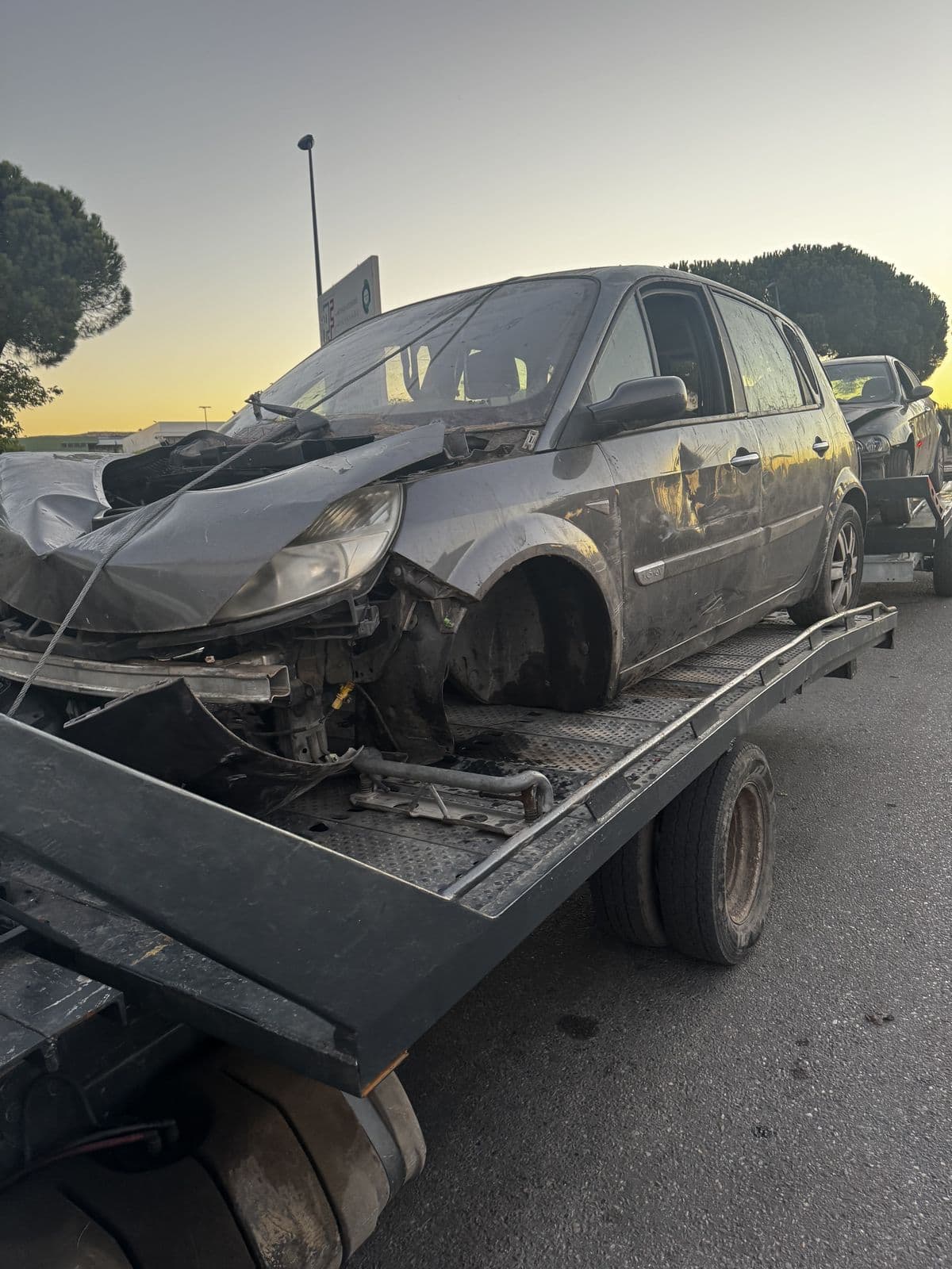 Monospace accidenté, avant enfoncé et roue arrachée, chargé sur le plateau au coucher du soleil